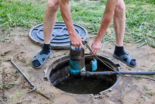 Plumber submerges wastewater pump into septic tank effluent to pumping sewage water before tank maintenance.