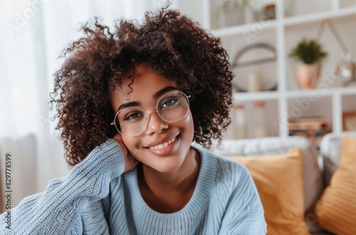 Retrato de una hermosa mujer latina auténtica con cabello afro, llevando un suéter azul claro y gafas. Ella mira a la cámara y sonríe.
 photo