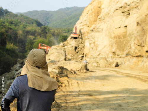 Contractor wearing ear neck flap cap supervises ongoing road construction project in the hills