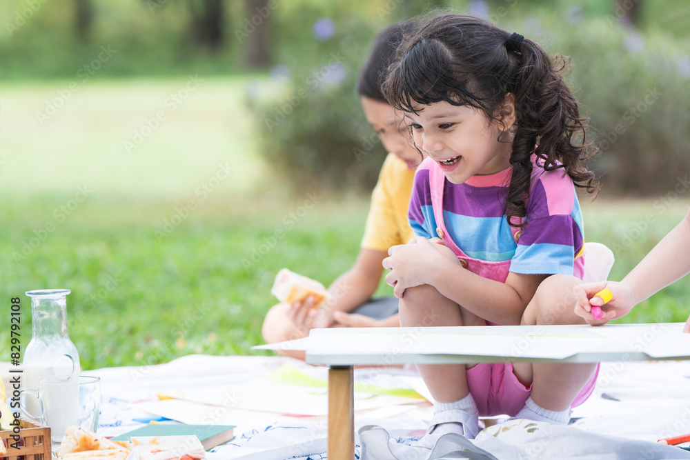 Happy Caucasian child girl with multiracial group of friends coloring with crayons on paper at park, sitting on grass. Little kid and friends have fun together outdoors activities. Creatives children Happy Caucasian child girl with multiracial group of friends coloring with crayons on paper at park, sitting on grass. Little kid and friends have fun together outdoors activities. Creatives children