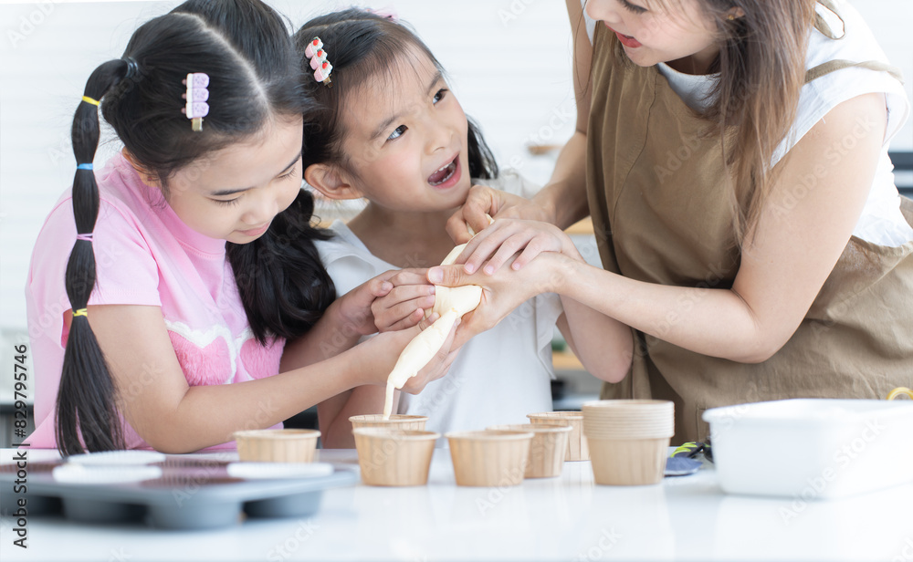 Mother and two daughters enjoy making cupcakes together at home kitchen. Mom and little child girl squeezing cake batter into cupcake paper cup, prepare for bake, smiling. Selective focus on hands Mother and two daughters enjoy making cupcakes together at home kitchen. Mom and little child girl squeezing cake batter into cupcake paper cup, prepare for bake, smiling. Selective focus on hands