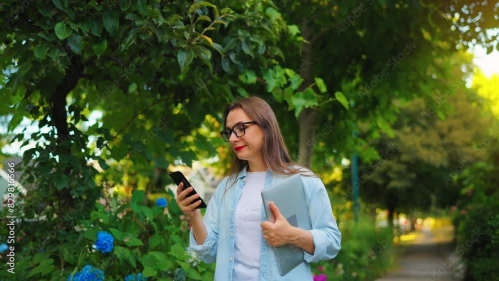 Woman with laptop and smartphone goes in the blooming garden Woman with laptop and smartphone goes in the blooming garden