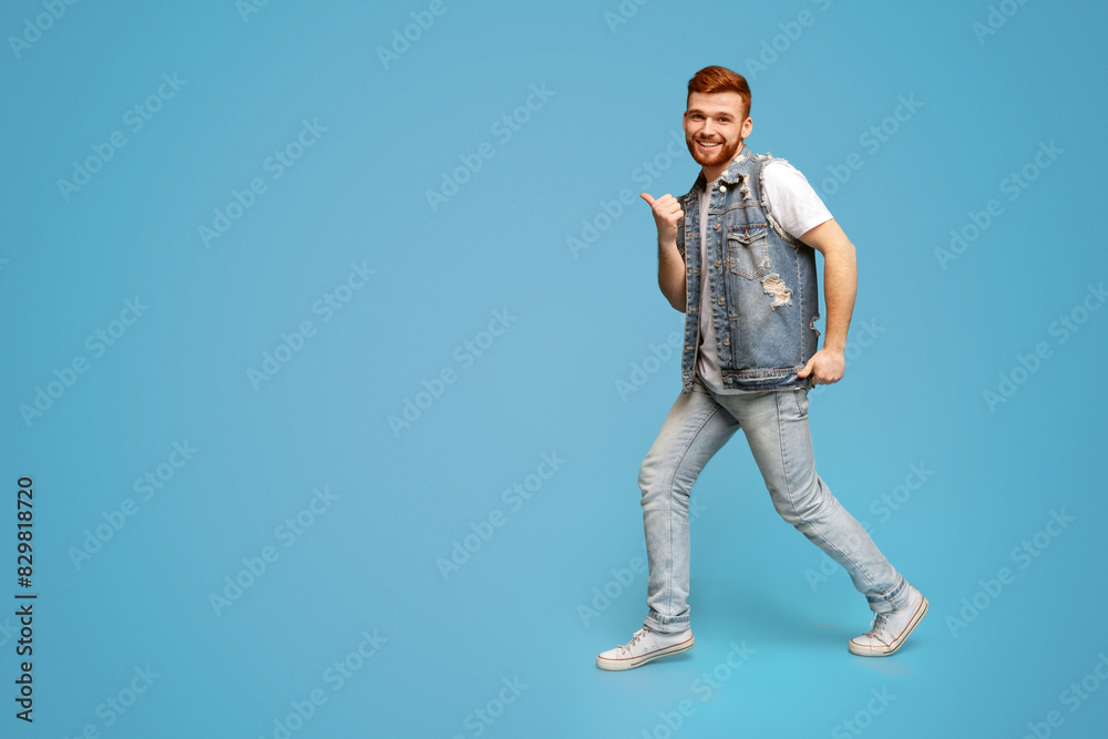 Naklejka premium Cool millennial man dancing with thumbs up gestures on blue background, studio, copy space, full length