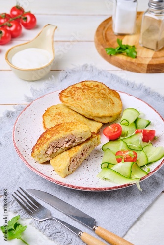 Potato pancakes stuffed with minced meat on a ceramic plate on a light wooden background. Served with fresh cucumber and cherry tomatoes. Belarusian cuisine.