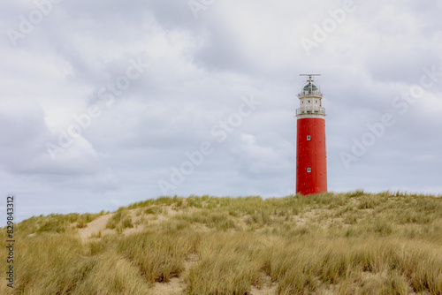 The Eierland Lighthouse on the northernmost top of the Dutch island of Texel  Red lighthouse tower on the sand dunes with european marram grass and cloudy sky as background  North Holland  Netherlands