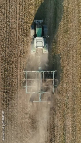 Countryside and agriculture, farm tractors plow the earth in field, dust in the field, view from height, vertical video.