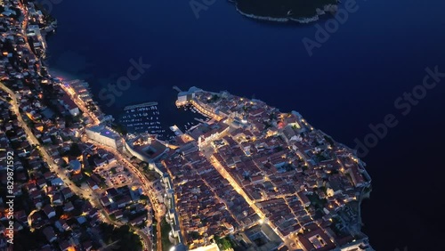 Amazing aerial panoramic video of the picturesque town of Dubrovnik with the old town, illuminated streets and buildings and marina with boats in blue hour after sunset. Top view with Lokrum island.