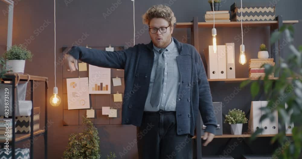 Loop portrait of joyful young businessman dancing enjoying music in modern office in evening. People and workplace fun concept.