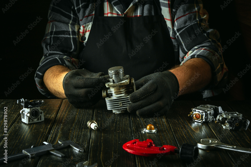 A foreman at a workbench in a workshop repairs the engine of a lawn mower after a breakdown. Replacing the piston in the engine cylinder A foreman at a workbench in a workshop repairs the engine of a lawn mower after a breakdown. Replacing the piston in the engine cylinder