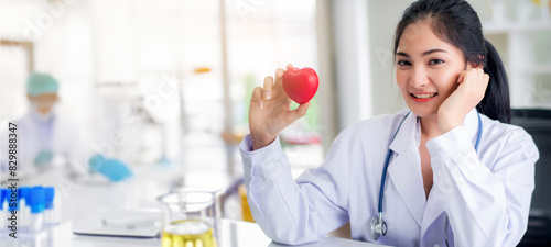 Smile beautiful young Asian doctor hold heart shape in hand standing at laboratory background	