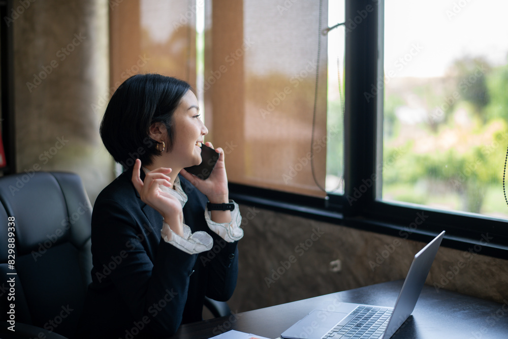 Obraz premium A woman is talking on her cell phone while sitting at a desk