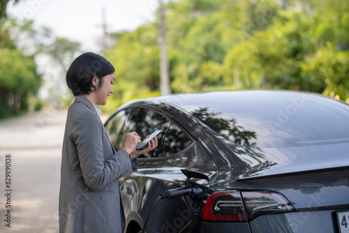 A woman is standing next to a black car with a charging station