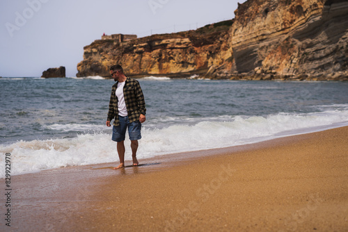A man in a shirt and shorts walks on the Nazaré Beach on an off-season spring day.