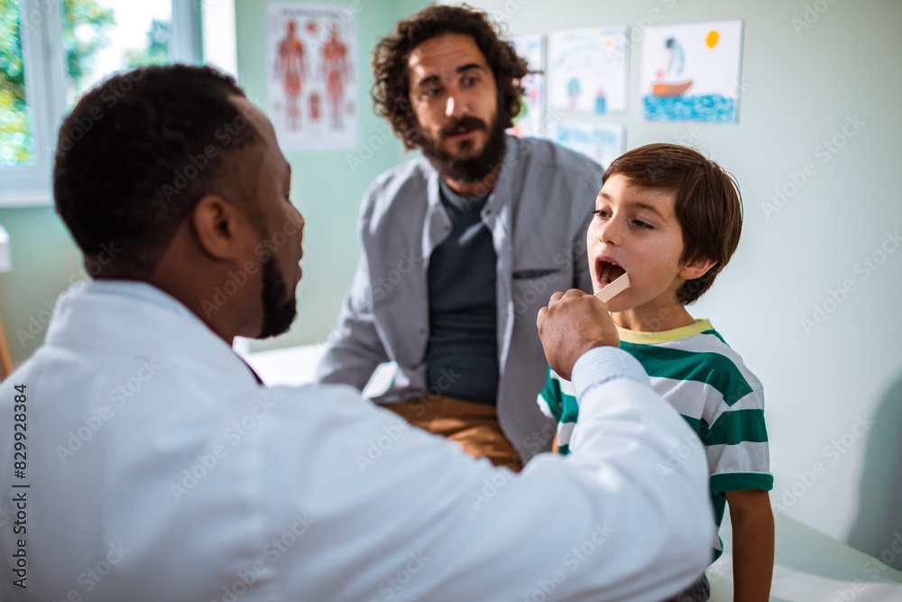 Pediatrician examining young boy's throat with father watching Pediatrician examining young boy's throat with father watching