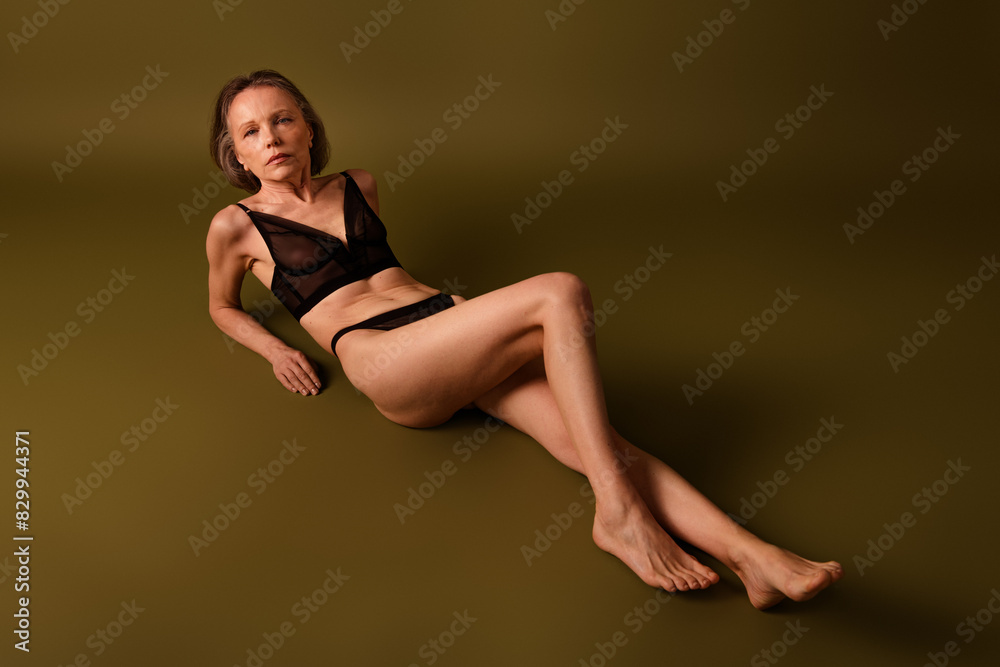 Obraz premium Full size photo of attractive senior woman lying floor seduce dressed black lingerie brown background no retouch self acceptance
