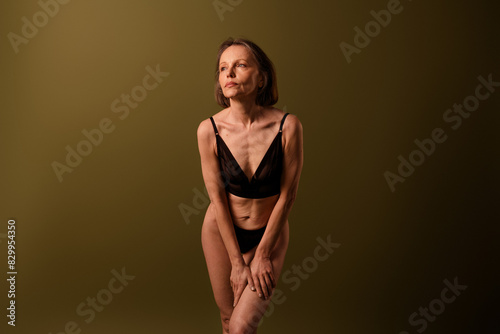 Photo of attractive senior woman look empty space touch hips dressed black lingerie brown background no retouch self acceptance © deagreez