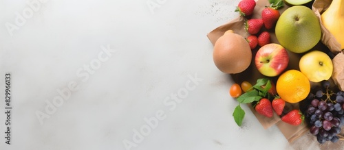 There is a copy space image featuring a flat lay of a shopping paper bag filled with nutritious fruits on a grey background
