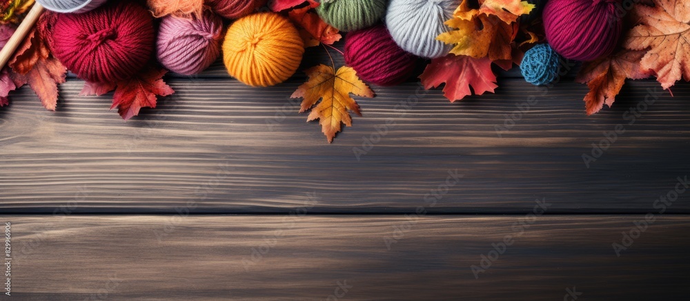 The DIY concept is showcased in a top down view of a wooden table adorned with balls of natural wool yarn and knitting needles Nearby vibrant autumn leaves add a touch of color to the composition The