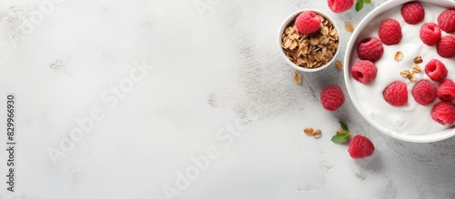 A healthy breakfast concept featuring a bowl of granola mixed with raspberries and Greek yogurt placed on a white marble table background The image is taken from a top down perspective with a flat la