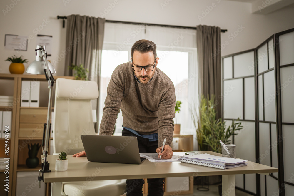 Adult businessman stand at office look and sign on document Adult businessman stand at office look and sign on document