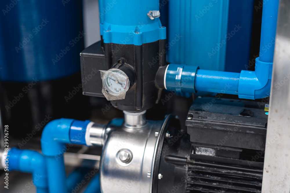 Close-up view of water refilling station equipment, featuring a pressure gauge and blue pipes, essential for water purification. Close-up view of water refilling station equipment, featuring a pressure gauge and blue pipes, essential for water purification.