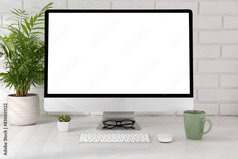 Fototapeta premium Office workplace with computer, cup, glasses, stationery and houseplant on light table near white brick wall