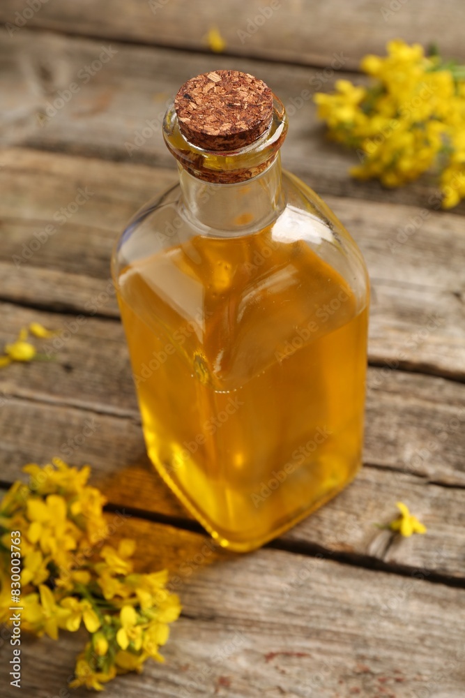 Rapeseed oil in glass bottle and beautiful yellow flowers on wooden table, closeup Rapeseed oil in glass bottle and beautiful yellow flowers on wooden table, closeup