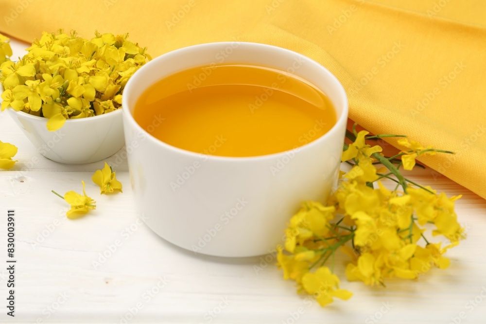 Rapeseed oil in bowl and beautiful yellow flowers on white wooden table Rapeseed oil in bowl and beautiful yellow flowers on white wooden table