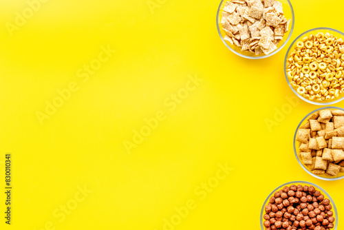 Various corn cereals in bowls on yellow background top view copyspace photo