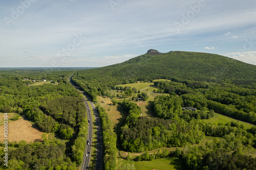 Highway Winds Around Green Forest that Surrounds Mountain Peak Under a Blue Sky