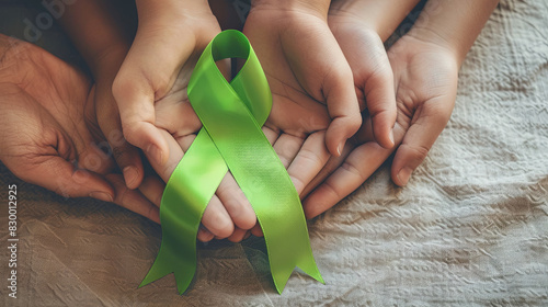 Hands of adults and children holding green health awareness ribbon. October 10, World Mental Health Day. February 4 is World Cancer Day photo