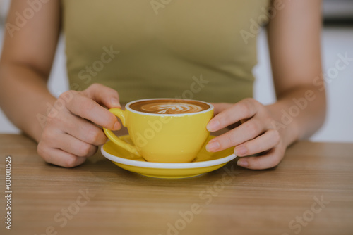Close-up shot of hot latte coffee cup on wooden table in woman s hand in cafe