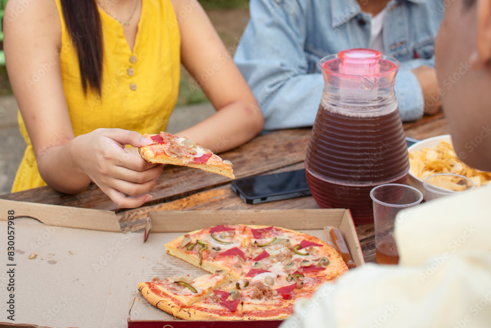 An anonymous young woman enjoys eating pizza with her boyfriend and friends during a casual outdoor picnic in a yard setting. An anonymous young woman enjoys eating pizza with her boyfriend and friends during a casual outdoor picnic in a yard setting.