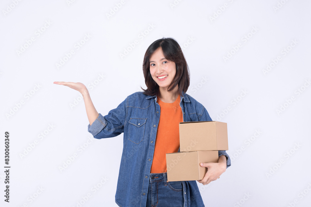 young asian woman wearing orange t-shirt and denim shirt holding parcel box isolated on white studio background, Delivery courier and shipping service concept.
