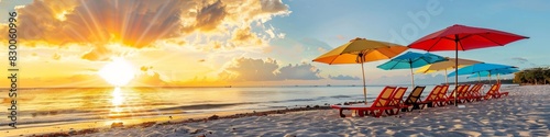 A beach with colorful umbrellas and lounge chairs set up for vacationers  facing the ocean as the sun sets. The tropical setting and the beautiful sunset create an inviting scene.