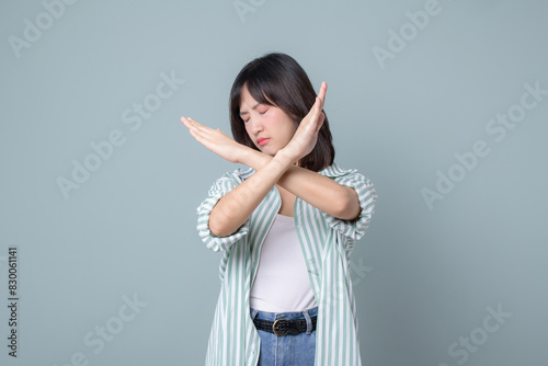 serious asian woman shows cross hands gesture, stop sign, taboo, disapproves bad action, stands in white and green shirt over pastel green background photo