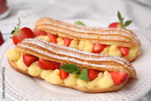 Delicious eclairs filled with cream, strawberries and mint on table, closeup