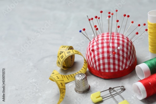 Checkered pincushion with pins and other sewing tools on grey table photo