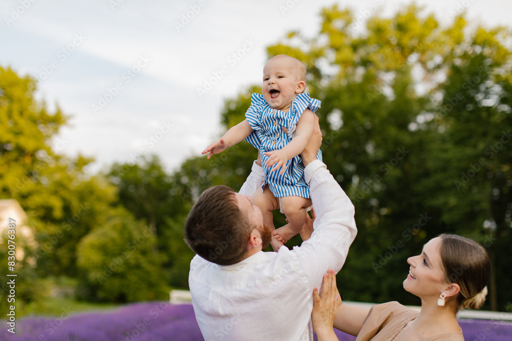 Father is lifting up his daughter in the air while they have fun together in the lavender field. Man and woman playing with his newborn baby girl in blue dress on the lavender field. Father is lifting up his daughter in the air while they have fun together in the lavender field. Man and woman playing with his newborn baby girl in blue dress on the lavender field.