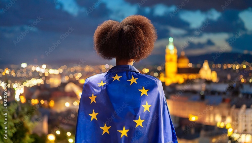 Fototapeta premium woman stands backwards with a developing European flag on her shoulders, against a blurred background of a night city
