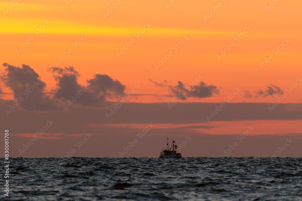 Seascape with smal fisher boat and red sky at dawn.