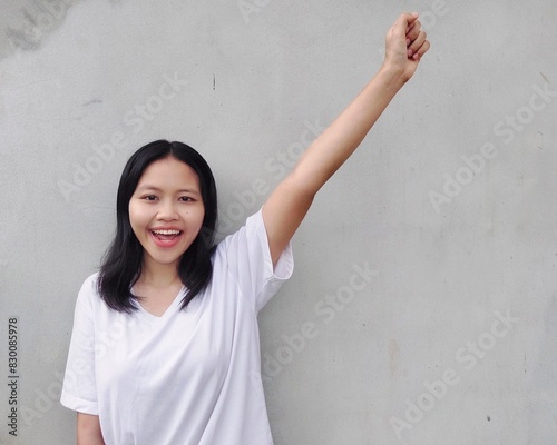 Portrait of Happy, excited, Joyful, Surprised, shocked Asian woman  raising her arm up Smiling and screaming for success, standing against grey background