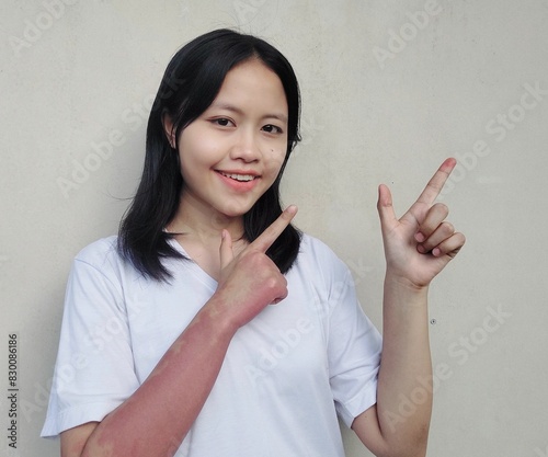 Image of portrait Waist up happy young woman standing isolated, smiling while pointing finger right, recommending product, Looking camera pointing, over grey background