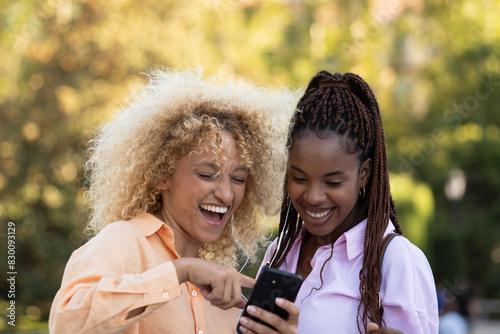 Two multiethnic girls laughing while checking something funny in the smartphone