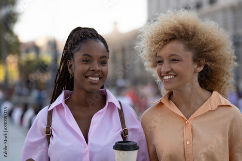 two multiracial girls friends together taking a break and holding a coffee cup outdoors