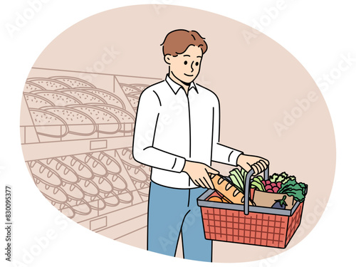 Man customer at grocery supermarket takes bread from shelf and puts it in basket of groceries. Guy visits supermarket or bakery buying fresh baguette and organic vegetables for preparing lunch.