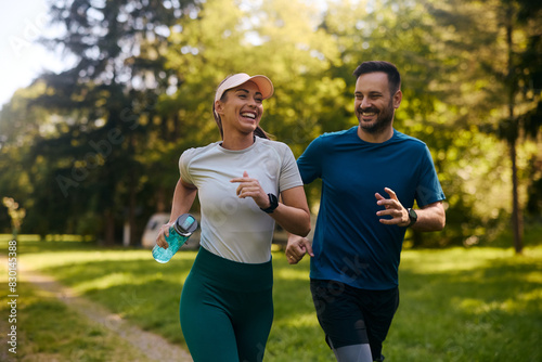 Fototapeta Naklejka Na Ścianę i Meble -  Cheerful athletic couple jogging through park.