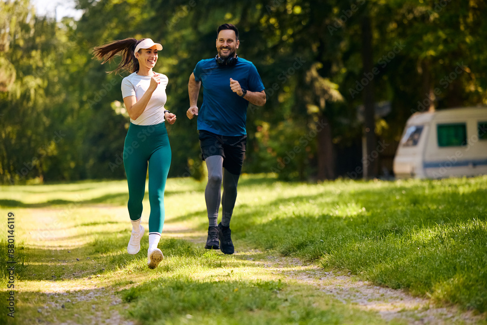 Happy athletic couple running while exercising in nature.