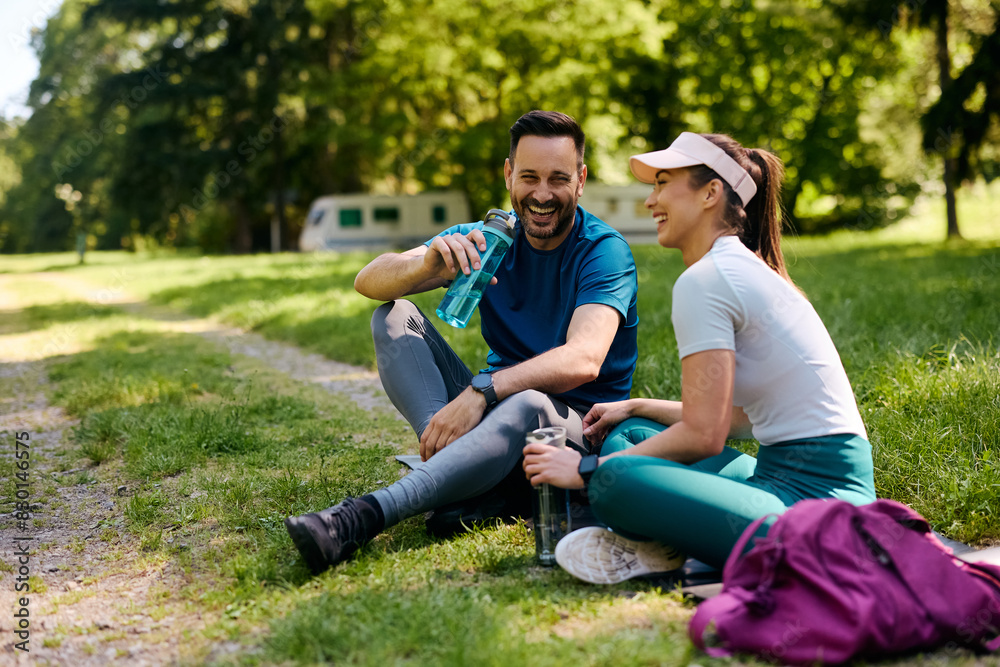 Cheerful athletic couple having water break while working out in park.