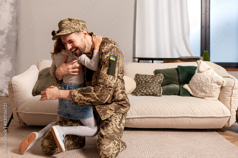 happy Ukrainian army soldier in camouflage uniform returned home and meets his daughter, the child runs to his military dad and hugs the veteran at home